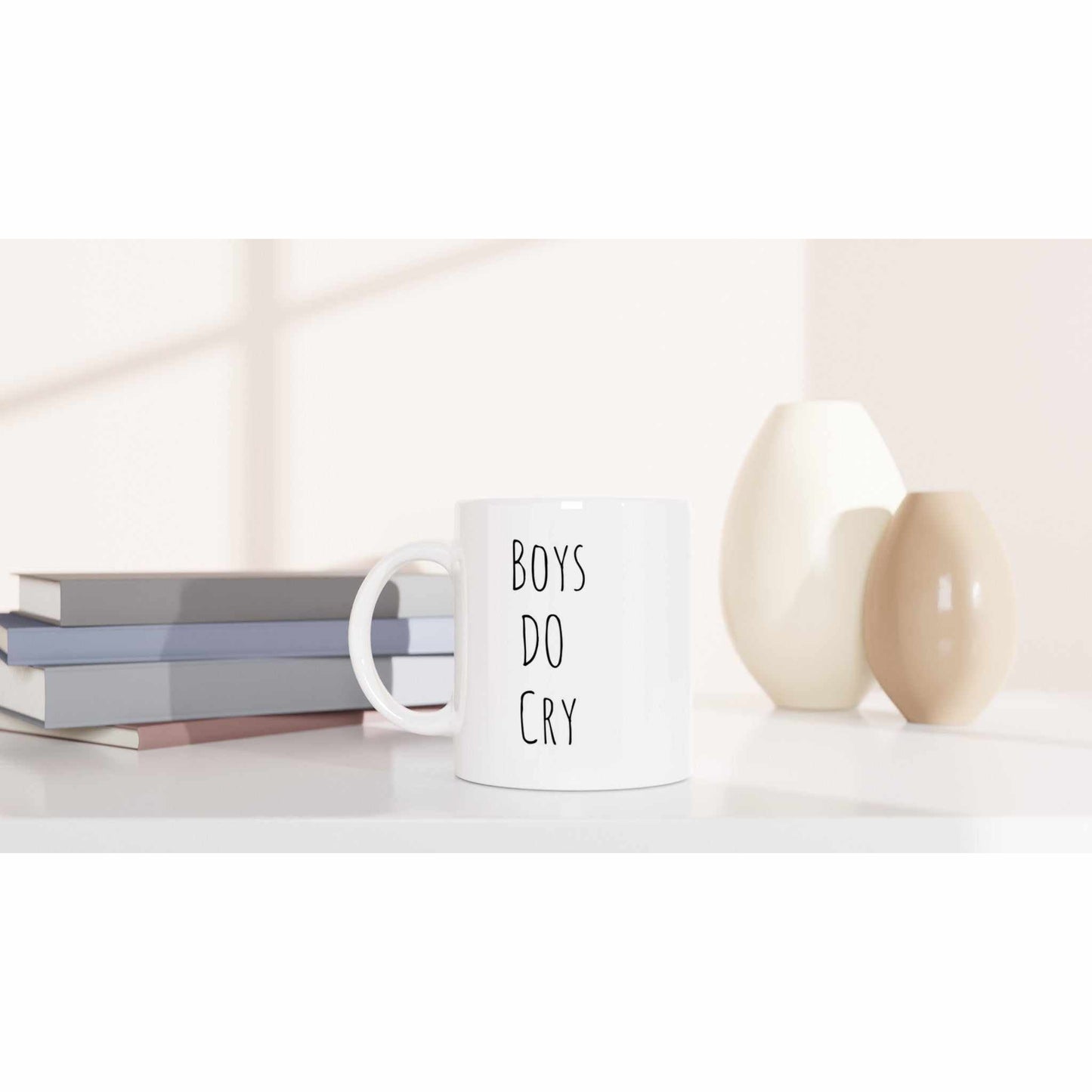 Boys Do Cry White 11oz Ceramic Mug on table with books and vases